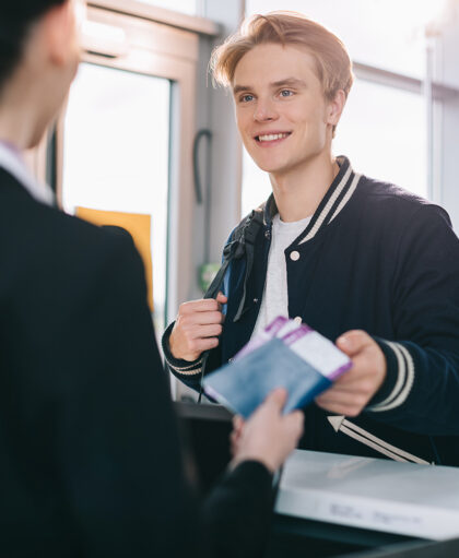 cropped shot of smiling young man giving passport to worker at check-in desk in airport